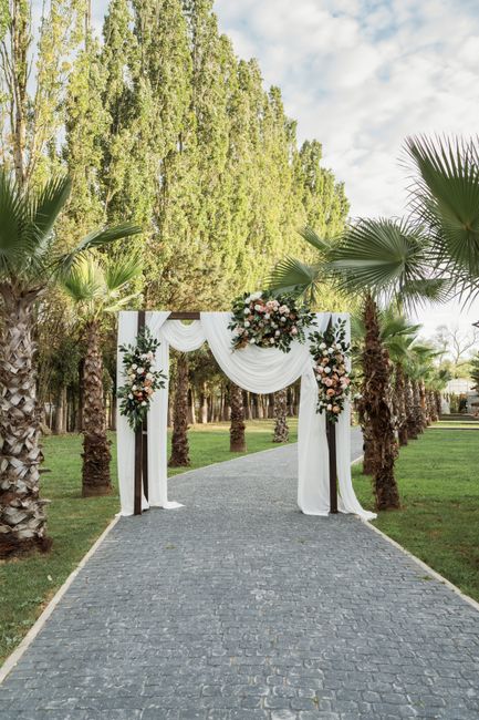 A floral arrangement featuring a large bouquet of mixed flowers including roses, peonies, and greenery in soft pink, white, and blush tones, beautifully displayed at a wedding ceremony set in an outdo